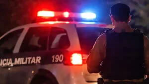 Viatura da Polícia Militar à noite em frente a residência, com dois policiais de costas, cena noturna. Imagem ilustra materia cureldade de animais em Ivaiporã