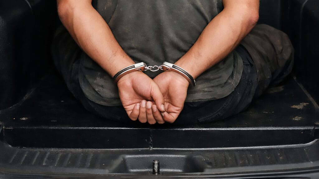 Homem algemado sentado no camburão de viatura policial,