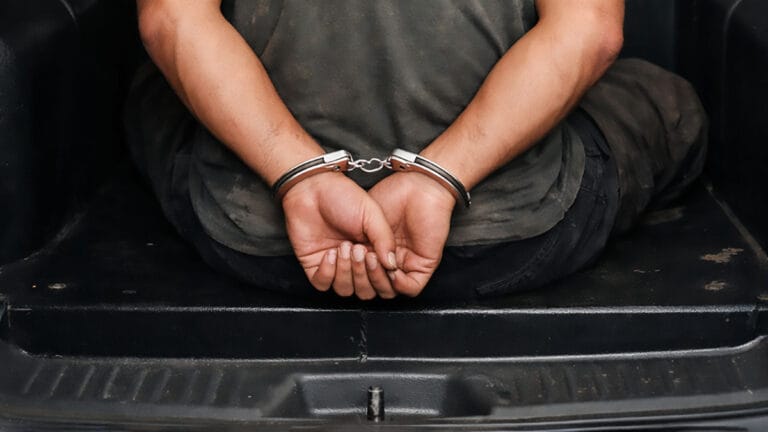 Homem algemado sentado no camburão de viatura policial,