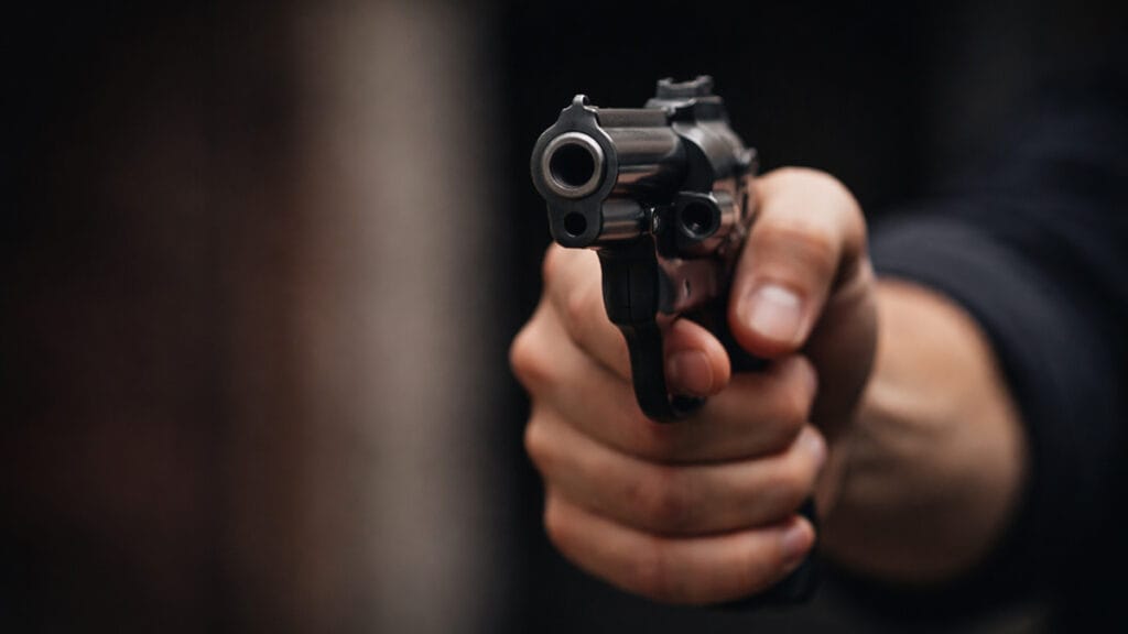 mão segurando um revólver apontado representando ameaça com arma de fogo