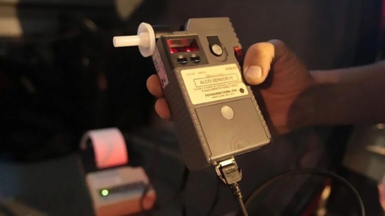 Mão de policial segurando aparelho de bafômetro durante fiscalização de trânsito à noite