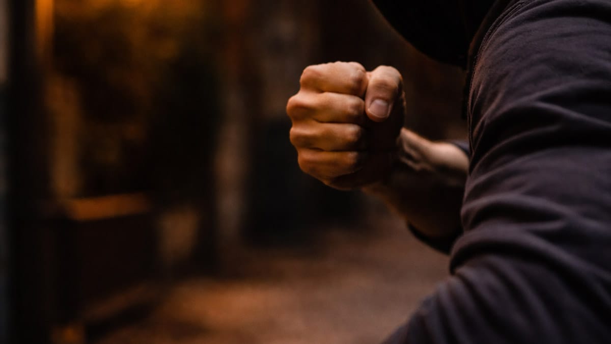 Mão fechada em gesto de ameaça em rua escura, imagem ilustrativa de agressão