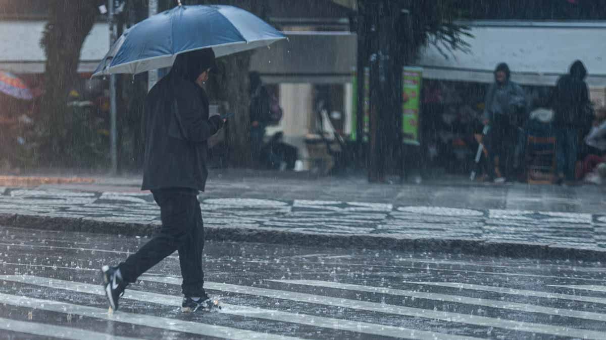 Pessoa atravessa faixa de pedestres sob chuva forte