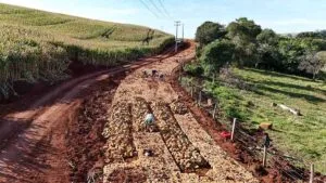 Obra de pavimentação com pedra irregular em estrada rural cercada por lavoura