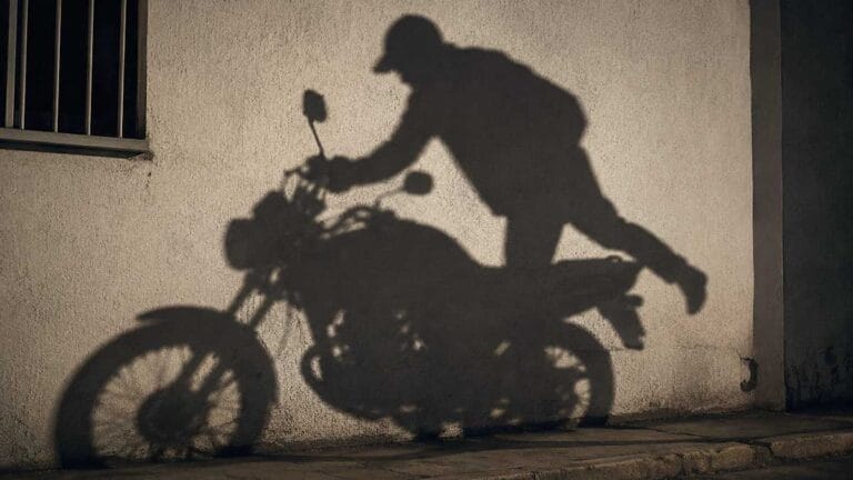 Sombra de suspeito subindo em motocicleta projetada na parede durante cena noturna que ilustra furto de moto.