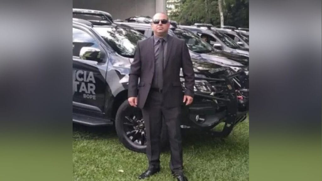 Sargento Rogério Knaipp de terno em frente a viaturas da Polícia Militar do Paraná