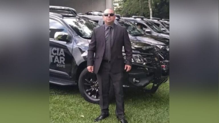 Sargento Rogério Knaipp de terno em frente a viaturas da Polícia Militar do Paraná