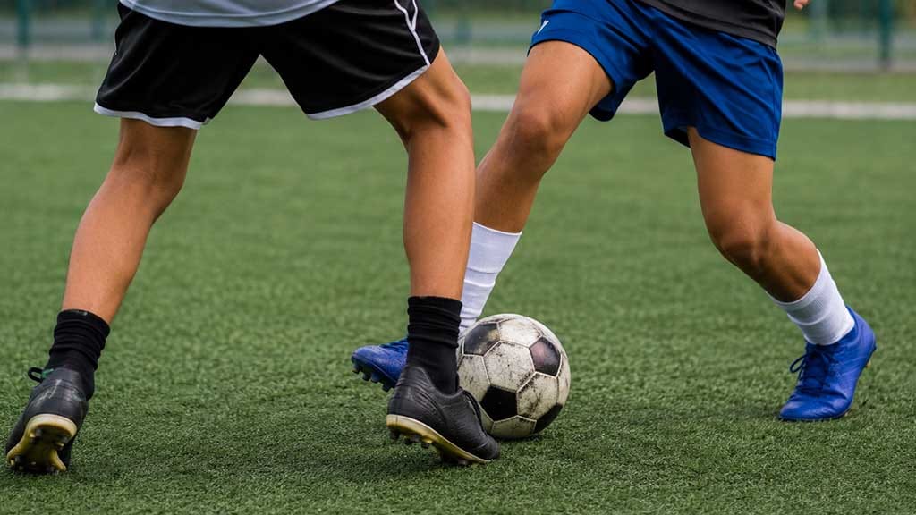 Adolescente é agredido após partida de futebol em Jardim Alegre Pernas de dois adolescentes disputam a bola durante uma partida de futebol em campo sintético,