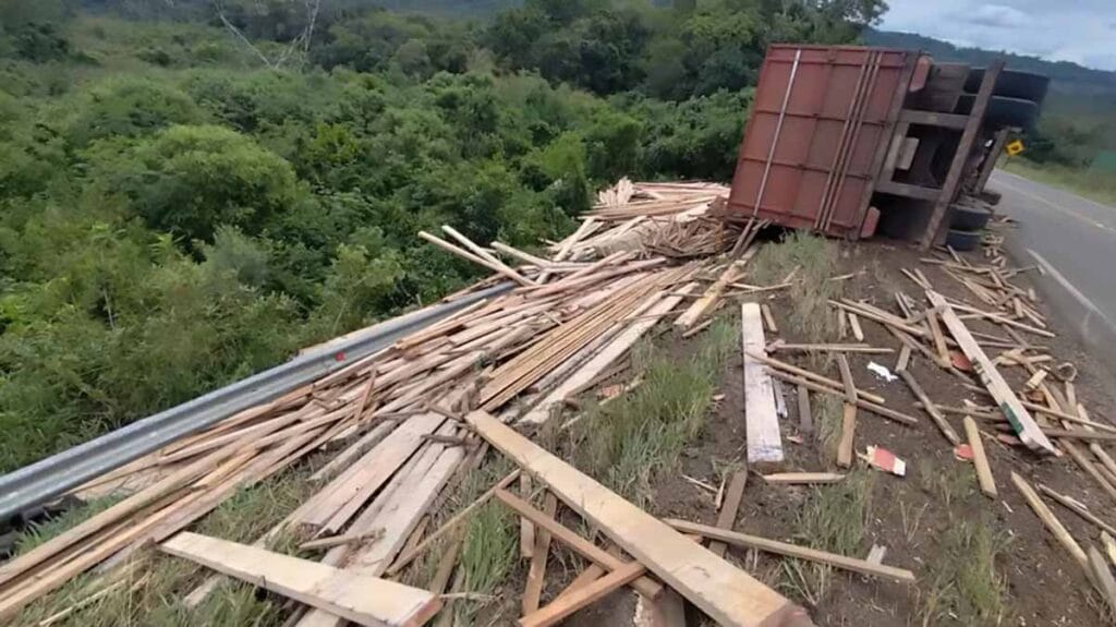 Caminhão carregado de madeira tomba após bater em ônibus e atinge carro na PR-459, em Reserva do Iguaçu