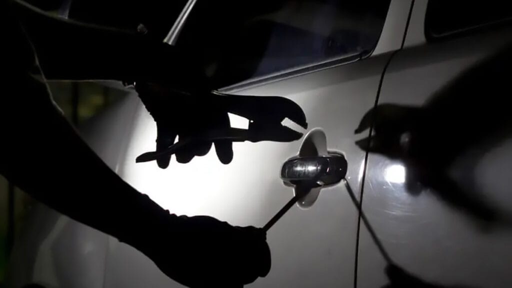 Pessoa tenta abrir a porta de um carro com ferramentas durante a noite