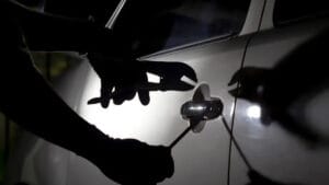 Pessoa tenta abrir a porta de um carro com ferramentas durante a noite