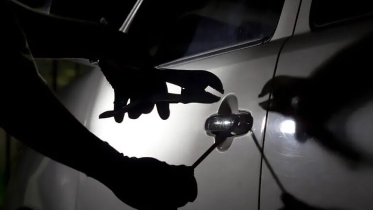 Pessoa tenta abrir a porta de um carro com ferramentas durante a noite