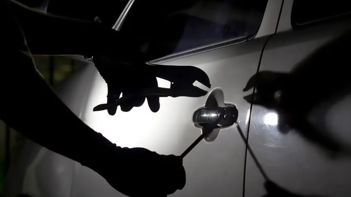 Pessoa tenta abrir a porta de um carro com ferramentas durante a noite